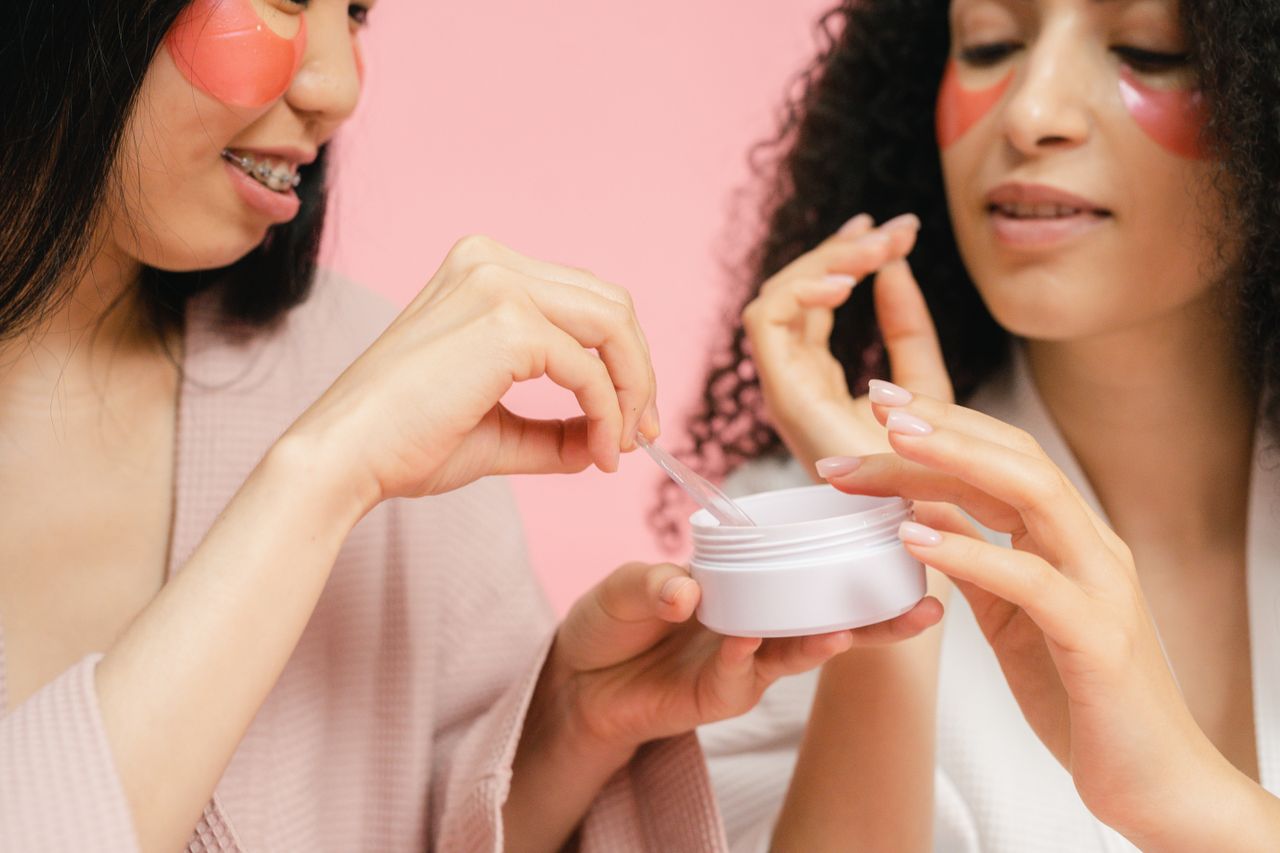 gallery-01 Two women in bathrobes applying skincare products with pink eye masks. Perfect for wellness and beauty themes.